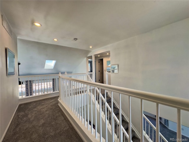 hallway with dark colored carpet and vaulted ceiling with skylight