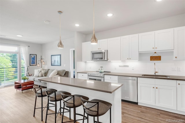 kitchen featuring white cabinetry, sink, appliances with stainless steel finishes, a breakfast bar area, and pendant lighting