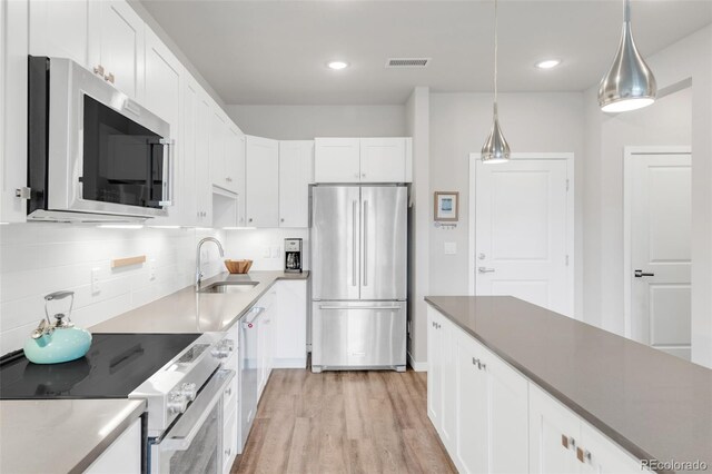 kitchen with stainless steel appliances, hanging light fixtures, sink, backsplash, and white cabinets