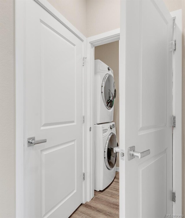 clothes washing area with stacked washing maching and dryer and light wood-type flooring