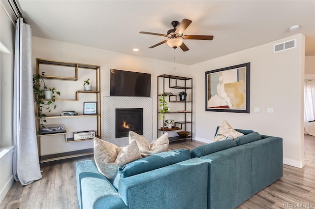 living room with hardwood / wood-style flooring, ceiling fan, and a tile fireplace