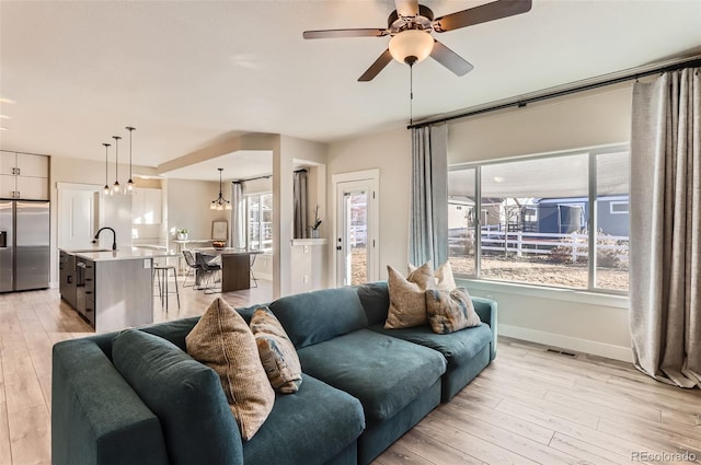 living room featuring sink, light hardwood / wood-style floors, a healthy amount of sunlight, and ceiling fan