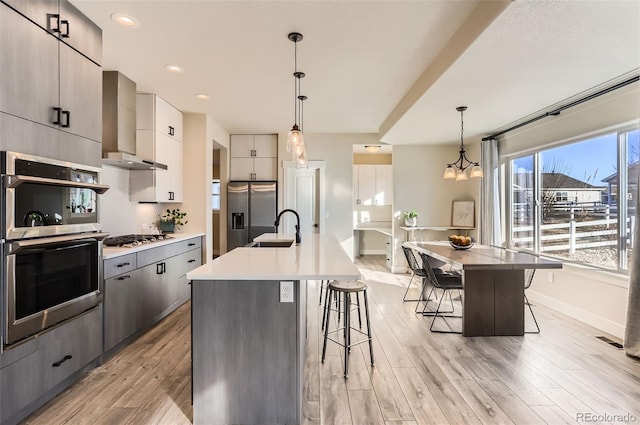 kitchen with wall chimney range hood, a kitchen breakfast bar, appliances with stainless steel finishes, and a center island with sink