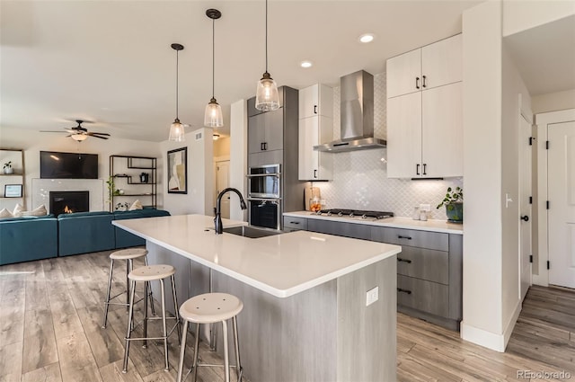 kitchen featuring decorative light fixtures, a kitchen bar, a kitchen island with sink, stainless steel appliances, and wall chimney range hood