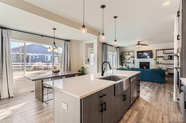 kitchen featuring an island with sink, sink, pendant lighting, and light wood-type flooring