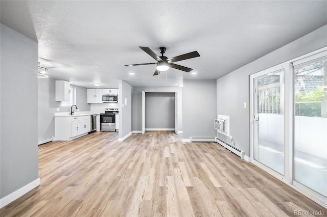 unfurnished living room featuring a baseboard heating unit, sink, ceiling fan, light wood-type flooring, and a textured ceiling