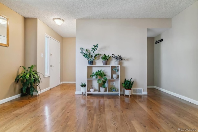 foyer entrance featuring baseboards, a textured ceiling, visible vents, and wood finished floors