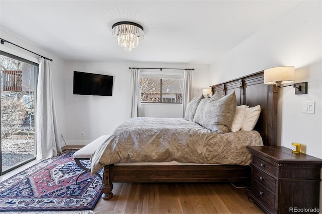 bedroom with access to exterior, a notable chandelier, wood finished floors, and baseboards