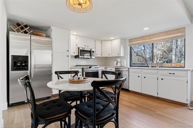 kitchen featuring white cabinets, light wood finished floors, backsplash, and stainless steel appliances