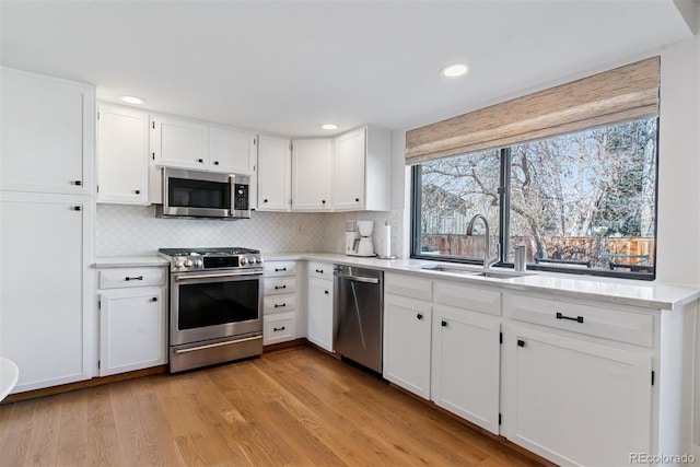 kitchen with light wood-type flooring, a sink, backsplash, stainless steel appliances, and white cabinets