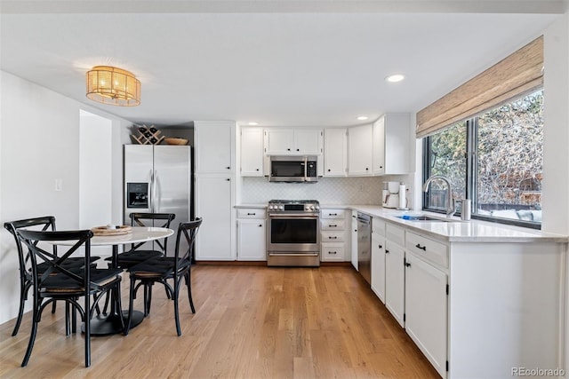 kitchen featuring light wood-style flooring, a sink, tasteful backsplash, stainless steel appliances, and light countertops