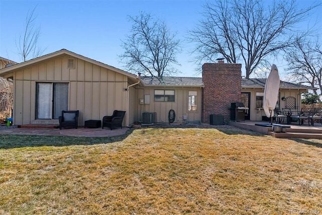 rear view of house featuring board and batten siding, central AC unit, a lawn, a chimney, and a patio area