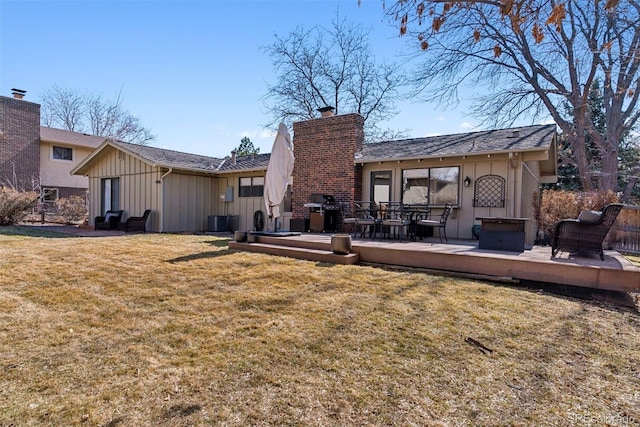 rear view of house featuring a deck, board and batten siding, a chimney, and a yard