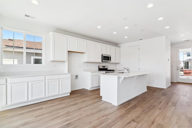 kitchen featuring sink, stainless steel appliances, a kitchen island with sink, white cabinets, and light wood-type flooring