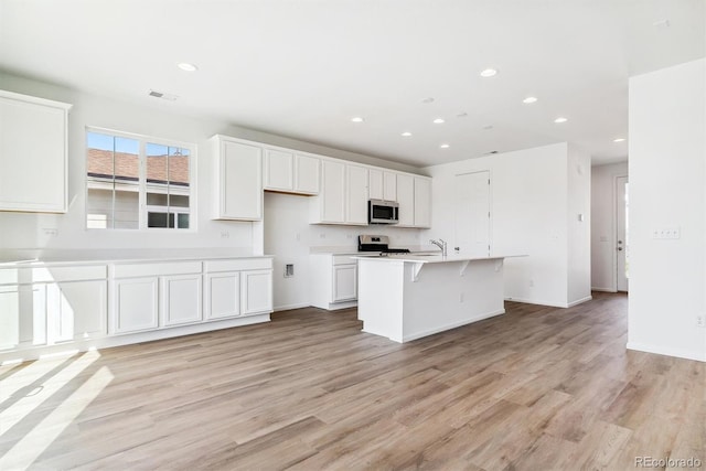 kitchen with white cabinets, light wood-type flooring, an island with sink, appliances with stainless steel finishes, and a breakfast bar area