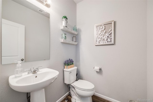 half bathroom with toilet, baseboards, a sink, and wood finished floors