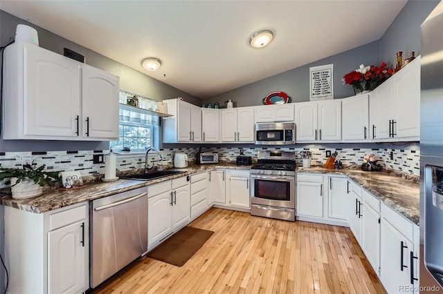 7716 Shenandoah Dr, Elizabeth, CO 80107 - kitchen featuring appliances with stainless steel finishes, a sink, white cabinetry, backsplash, and vaulted ceiling