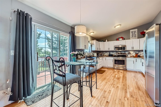 7716 Shenandoah Dr, Elizabeth, CO 80107 - kitchen with appliances with stainless steel finishes, tasteful backsplash, lofted ceiling, white cabinets, and light wood-style flooring