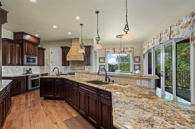 2378 Plumb Pl, Erie, CO 80516 - kitchen with custom range hood, appliances with stainless steel finishes, backsplash, wood finished floors, and light stone countertops