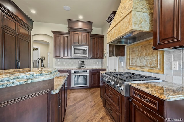 2378 Plumb Pl, Erie, CO 80516 - kitchen with stainless steel appliances, premium range hood, light stone counters, and arched walkways
