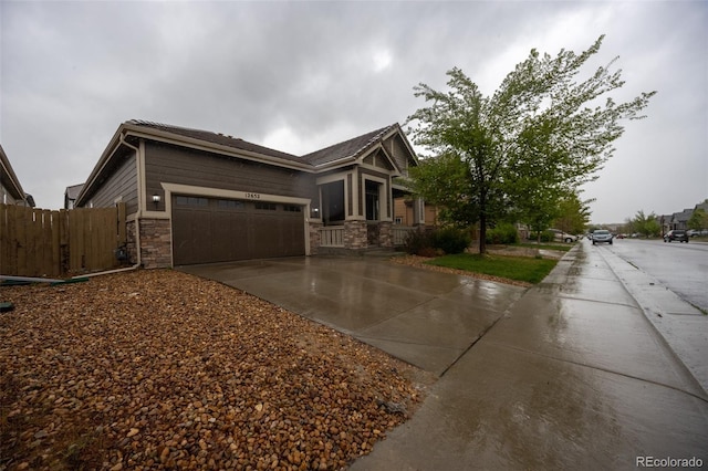 view of side of home featuring driveway, stone siding, a garage, and fence