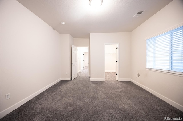 unfurnished bedroom with dark carpet, baseboards, and a walk in closet