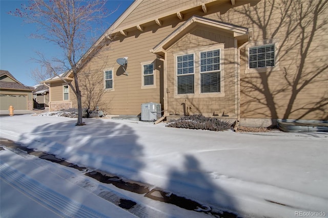 view of snow covered exterior with cooling unit and a garage