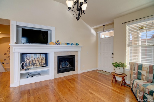 living room with a tiled fireplace, vaulted ceiling, plenty of natural light, and wood finished floors