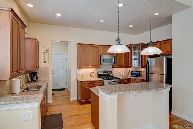 kitchen featuring appliances with stainless steel finishes, light stone countertops, light wood-type flooring, and a sink