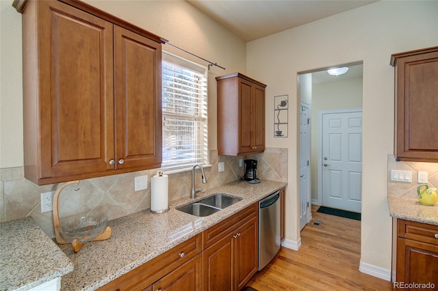 kitchen with dishwasher, light stone counters, brown cabinets, and a sink