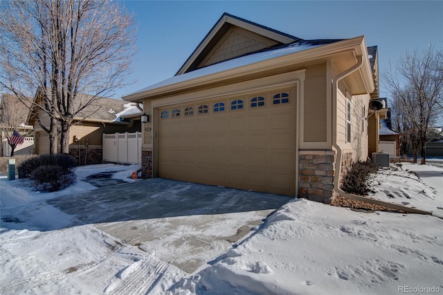 snow covered property featuring stone siding, driveway, an attached garage, and central AC