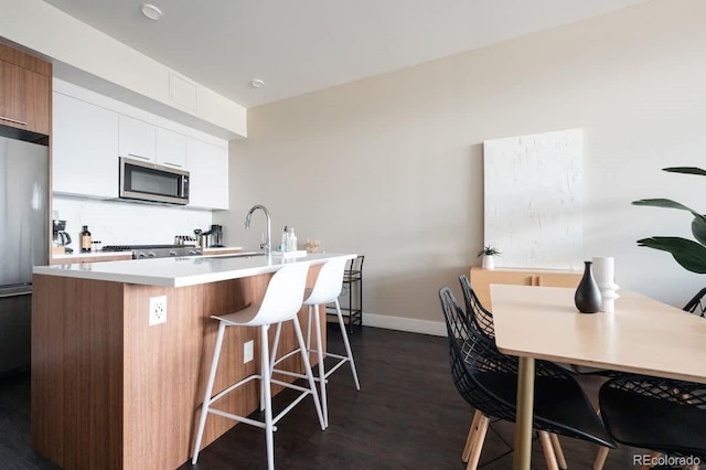 kitchen featuring a sink, white cabinetry, a kitchen breakfast bar, light countertops, and appliances with stainless steel finishes