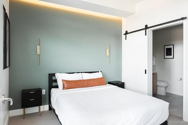 bedroom with ensuite bathroom, a barn door, and baseboards