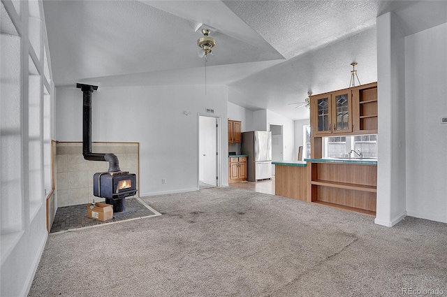 unfurnished living room with a textured ceiling, a wood stove, carpet floors, and lofted ceiling