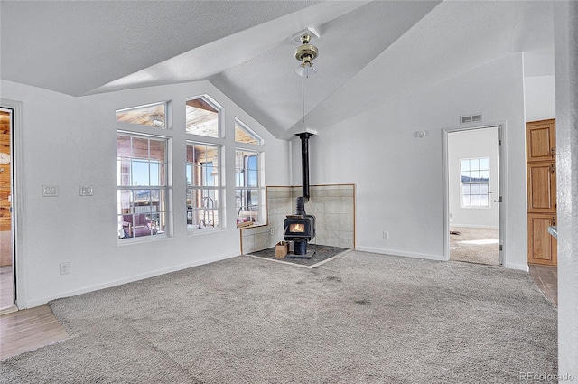 unfurnished living room with a wood stove, lofted ceiling, carpet floors, and a textured ceiling