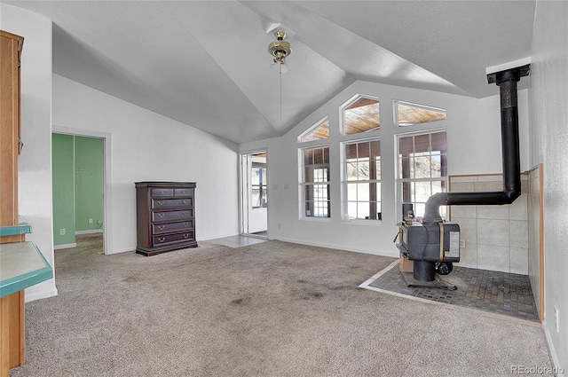 unfurnished living room featuring carpet flooring, a wood stove, a textured ceiling, and vaulted ceiling