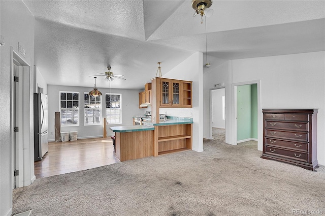 kitchen featuring stainless steel appliances, kitchen peninsula, pendant lighting, vaulted ceiling, and light carpet