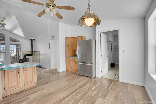 kitchen featuring a wood stove, light hardwood / wood-style flooring, vaulted ceiling, light brown cabinetry, and stainless steel refrigerator