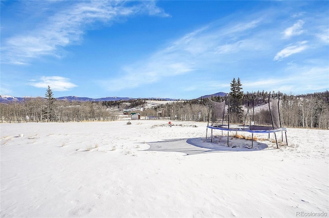 yard covered in snow featuring a mountain view and a trampoline