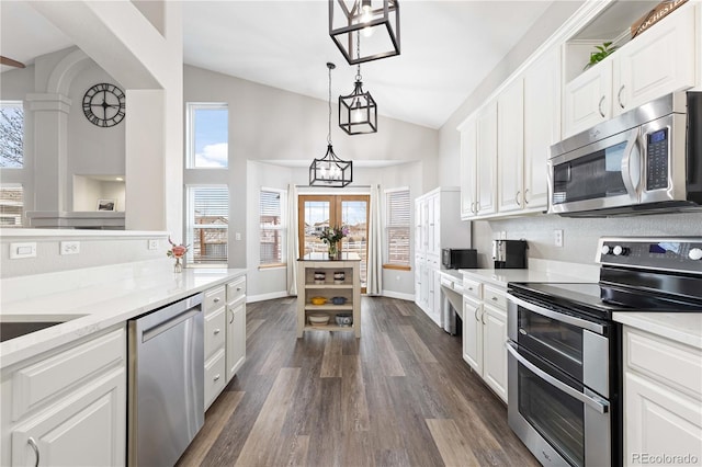 kitchen with appliances with stainless steel finishes, decorative light fixtures, white cabinets, light stone counters, and dark wood-type flooring