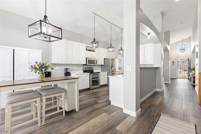 kitchen featuring a towering ceiling, stainless steel appliances, decorative light fixtures, and white cabinets