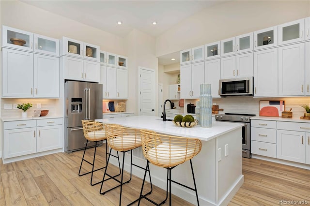 kitchen with light wood finished floors, a center island with sink, decorative backsplash, and stainless steel appliances
