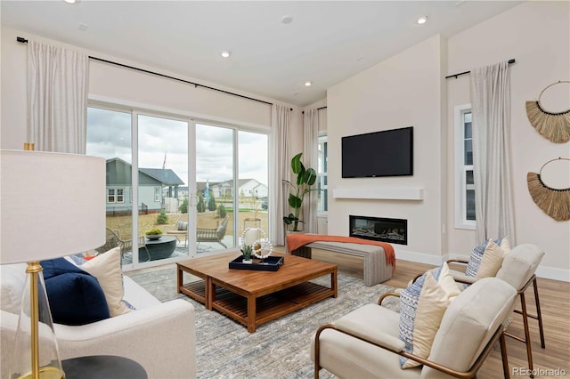 living room featuring baseboards, a glass covered fireplace, recessed lighting, and light wood-type flooring