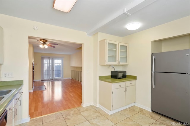 kitchen featuring glass insert cabinets, freestanding refrigerator, light countertops, white cabinetry, and black microwave