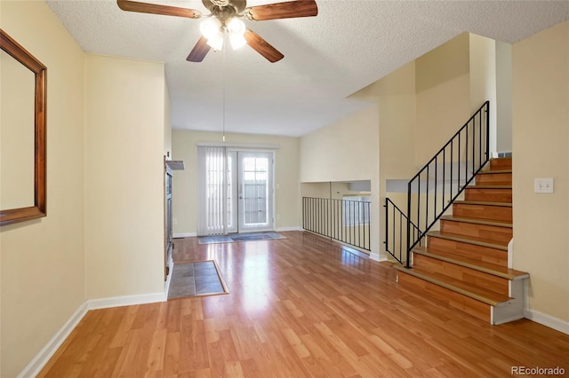 entrance foyer featuring a textured ceiling, light wood finished floors, stairway, and baseboards