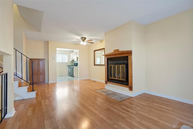 unfurnished living room with light wood-type flooring, a glass covered fireplace, baseboards, and stairs