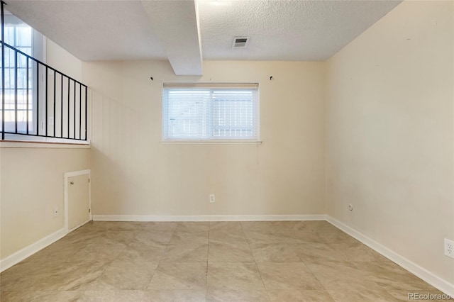 spare room with a textured ceiling, light tile patterned floors, visible vents, and baseboards