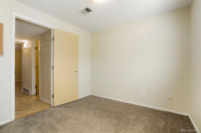 carpeted spare room featuring visible vents, a textured ceiling, and baseboards