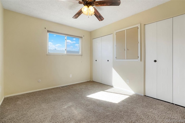 unfurnished bedroom with carpet floors, a textured ceiling, and multiple closets