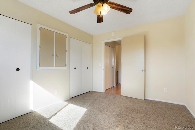 unfurnished bedroom with multiple closets, light carpet, and a ceiling fan